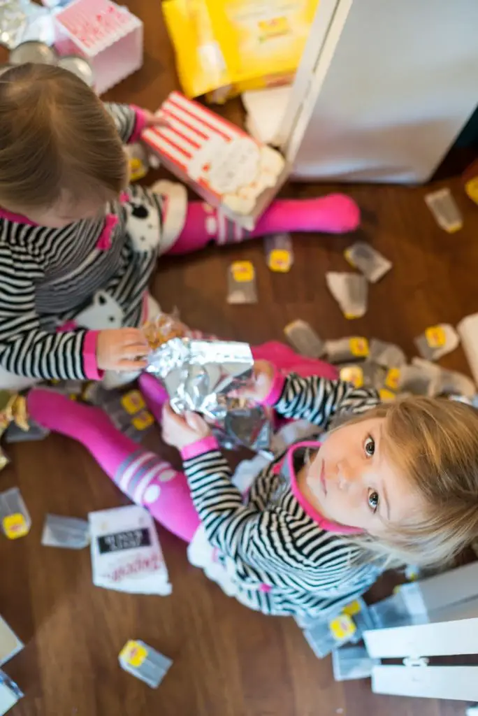 Two Toddler Girls Making A Mess With Tea Bags And Wrappers On The Kitchen Floor